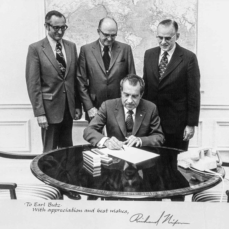 President Nixon signing the Act at a table surrounded by 3 other men.