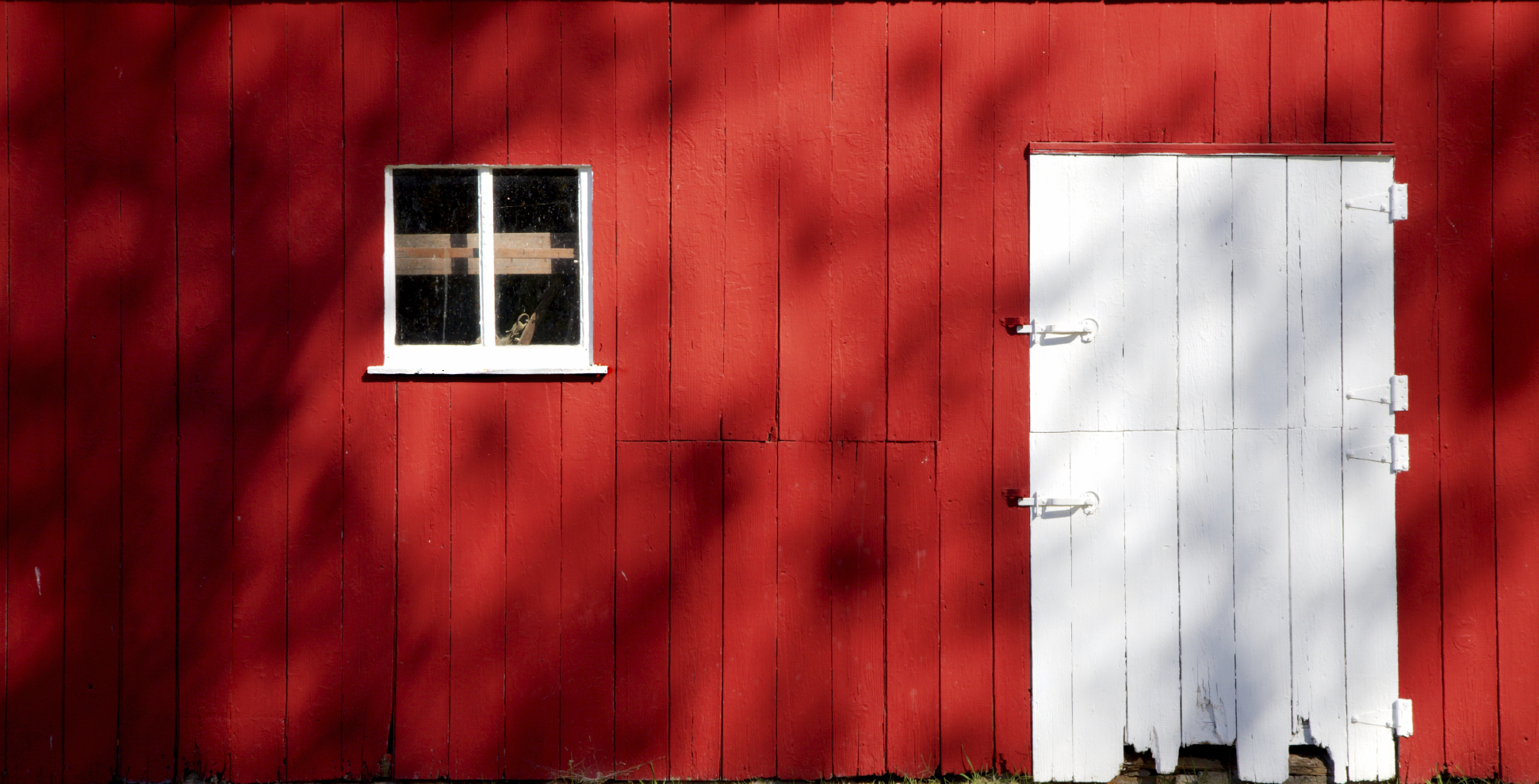 A wall of a red barn with a white door. 